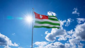 Abkhazian flag waving on pole, bright sun in the blue summer sky on the background