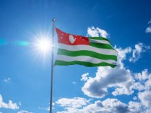 Abkhazian flag waving on pole, bright sun in the blue summer sky on the background